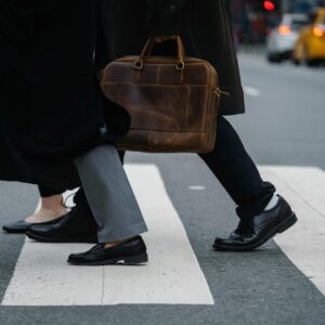 Side view of crop unrecognizable coworkers in formal wear with leather briefcase crossing urban road