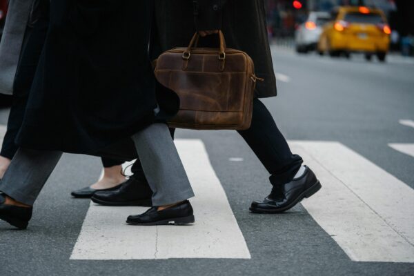 Side view of crop unrecognizable coworkers in formal wear with leather briefcase crossing urban road